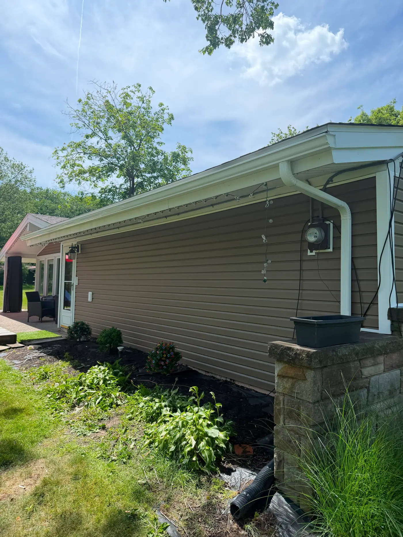 A new seamless gutter and downspout run cleanly fastened to tan siding.