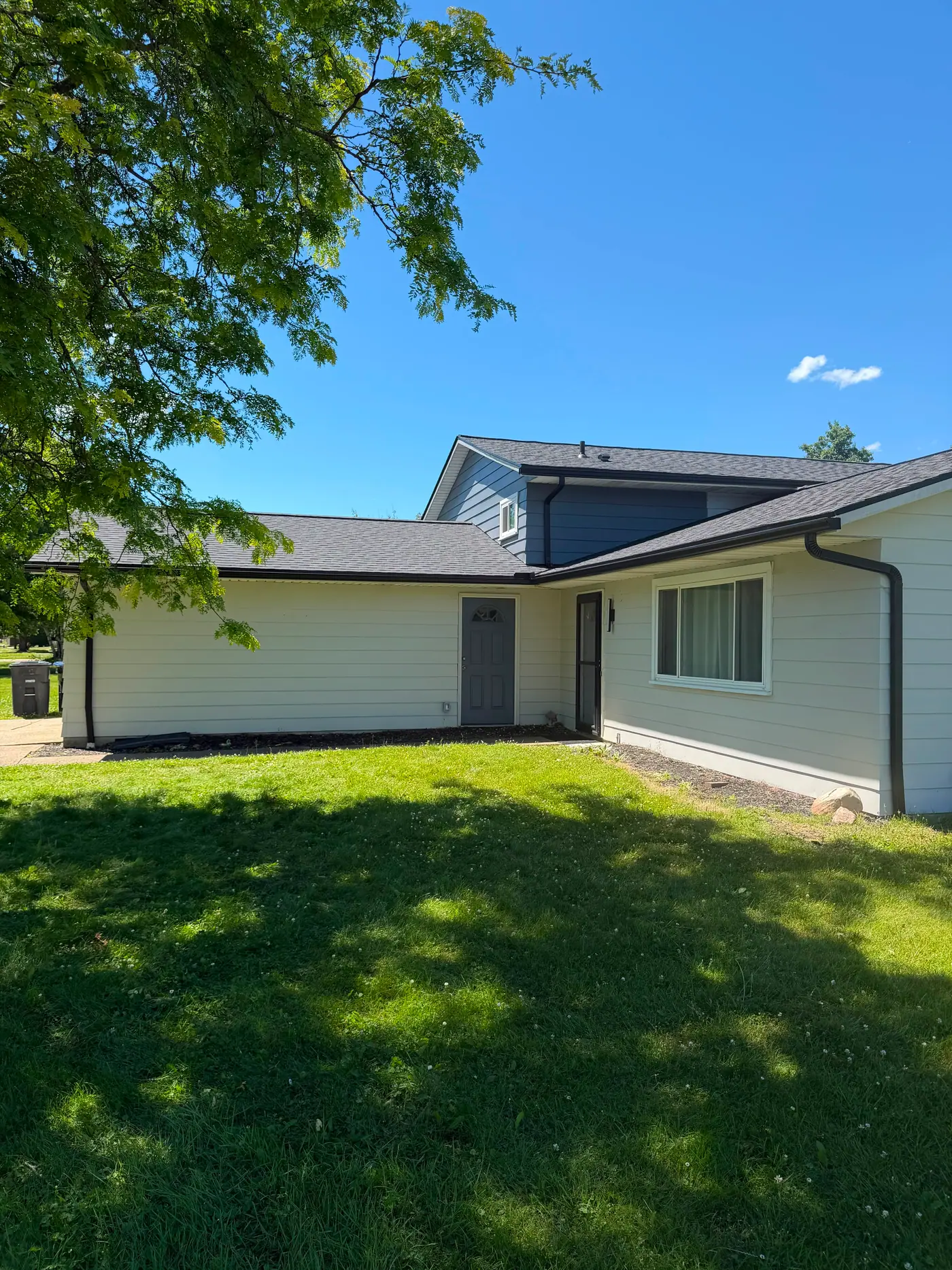 A cream ranch home with a clean new dark shingle roof and black gutters.